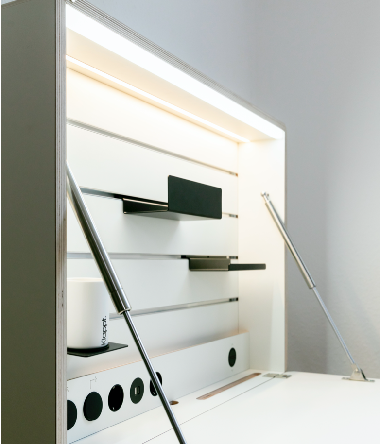 Ein weißer Klappt. ist geöffnet und mit Accessoires in der Rückwand ausgestattet. Das Tageslicht ist angeschaltet. Die Bremsklappenhalter, die schwarzen Lichtschalter, Steckdosen und USB-Steckdosen sind gut sichtbar.